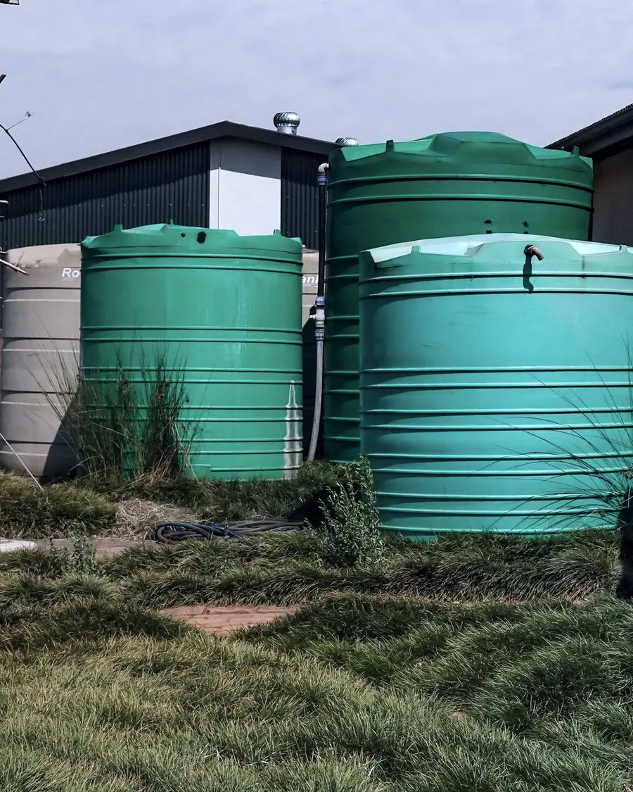 Two green poly water tanks standing on gravel beside a shed